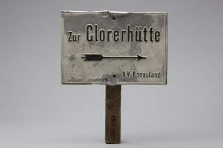 Altes, abgenutztes Schild mit der Aufschrift „Zur Glorerhütte“ und einem Pfeil nach rechts, befestigt an einem Holzstab.