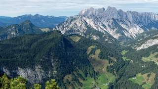 Blick von einem Berg ins Tal, das vor allem von Wald geprägt ist. Gegenüber fällt der Blick auf den Gebirgszug der Leoganger Steinberge.