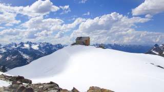 Hütte mit letzten Schneefeldern vor weiß-blauem Himmel