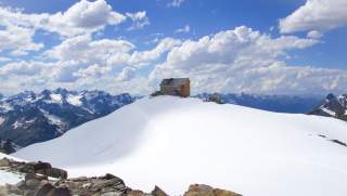 Hütte mit letzten Schneefeldern vor weiß-blauem Himmel