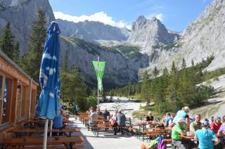 Viele Menschen sitzen auf der Terrasse der Höllentalangerhütte bei sonnigem Wetter.