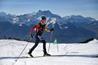 Skimo Athlet auf Schnee unterwegs, mit Gipfeln im Hintergrund
