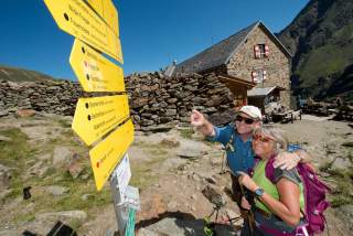 Zwei Menschen stehen vor Hütte und planen Tour anhand von Wegweisern