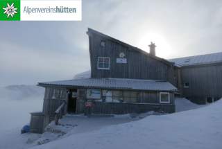 Hochwinter auf der Simonyhütte. Das Tal ist wolkenverhangen, die Sonne scheint diffus durch Schleierwolken. Es ist sichtbar kalt.