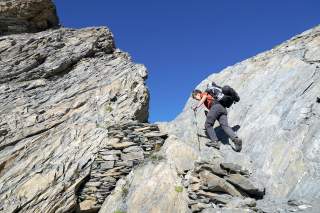 Bergwanderin im steilen Aufstieg zu einem felsigen Übergang.