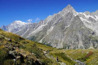 Wanderin auf einem Panoramaweg mit Blick auf die steilen Felswände der Grandes Jorasses und den vergletscherten Mont Blanc im Hintergrund