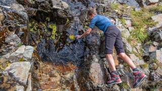 Bergsteigerin befüllt ihre Trinkflasche an einer Quelle-