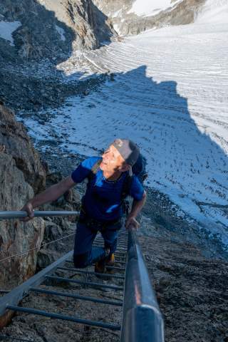 Bergsteiger steigt die letzten Meter zur Bertolhütte über eine Eisenleiter hinauf..