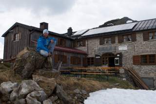 Hüttenwirt sitzt auf Stein vor Hütte