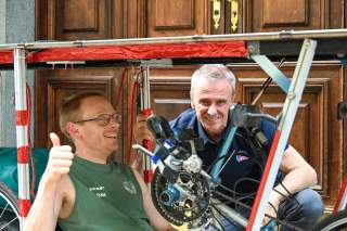 Sebastian Depke sitzt auf seinem Handbike mit Solardach. Dahinter hockt Marco Scolaris.