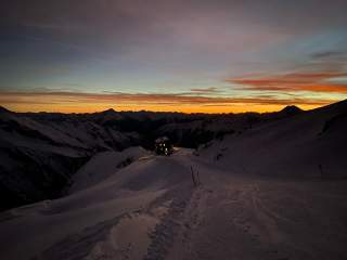 Beleuchtete Hütte am Rande der Skipiste im letzten Abendlicht und traumhaften Abendrot.