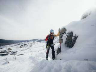 Die Athletin Helena Euringer auf der schneebedeckten Strecke, neben ihr Felsen und im Hintergrund das schneebedeckte Skigebiet.
