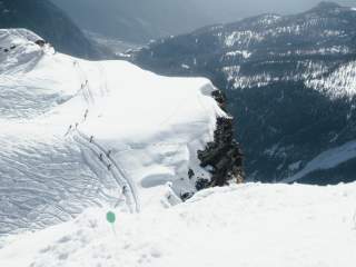 Man sieht schneebedeckte Berge und eine Spur in der Athleten gehen. Das Bild wurde von weiter oben aufgenommen.