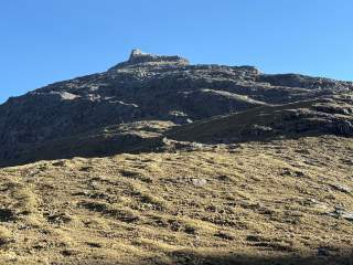 Berg mit felsigem Gipfel und grasbewachsenem Hang unter klarem blauem Himmel.