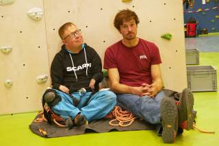 Paraclimber und Routenschrauber sitzen auf einem Seilsack an die Kletterwand gelehnt.