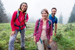 Zwei junge Frauen und ein junger Mann auf einem Wanderweg in den Bergen.