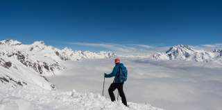 Ein Skifahrer schaut vom Berg hinab. Das Tal ist wolkenverhüllt.