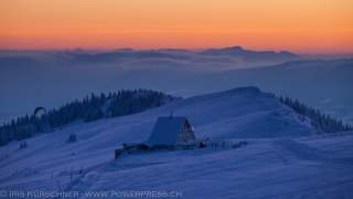 Sonnenuntergang über der Schneelandschaft. Eine Hütte steht in der Mitte, sie ist vereist.