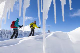 Zwei Menschen auf Langlaufski. Blick durch die Eiszapfen auf eine Winterlandschaft.