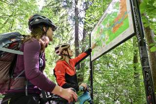 Zwei Mountainbikerinnen stehen vor einer Ausschilderung von Wegen des Isartaltvereins