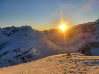 Sonne geht hinter verschneiten Berggipfeln unter