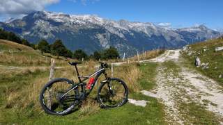 Mountainbike steht an Zaun neben Bergweg, Blick auf Berge