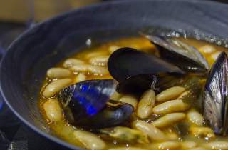 Ein Teller mit Eintopf aus weißen Bohnen und Muscheln in Großaufnahme