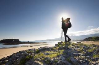 Person mit Rucksack steht an Strand in der Sonne