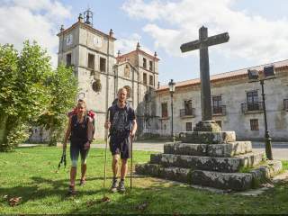 Wanderpaar läuft über eine Wiese vor einem alten Kloster.