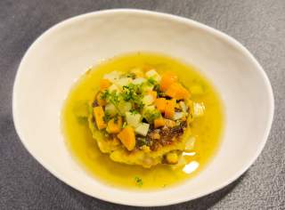 Suppe mit einem Kaspressknödel, garniert mit gewürfeltem Gemüse und frischen Kräutern in einer weißen Schale.