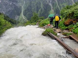 Zwei Leute wandern im Regen an Bergbach entlang