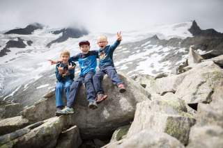 Drei Jungs sitzen auf großem Stein vor Gletscher