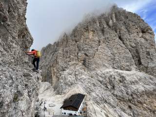 Mensch auf Klettersteig oberhalb von Berghütte