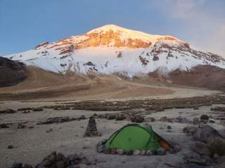 Ein Zelt steht am Fuße eines Berges. Die ersten Sonnenstrahlen erleuchten den mit Schnee bedeckten Gipfel.