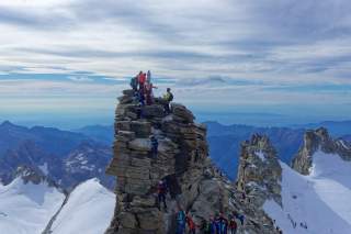 Bergsteigergruppe klettert auf einen felsigen Gipfel mit schneebedeckten Bergen im Hintergrund.