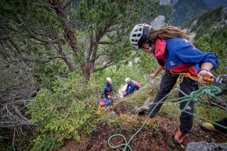 Teamarbeit bei der Bergrettung: Einsatzkräfte versorgen eine verletzte Person und bereiten mit Seiltechnik den sicheren Abtransport vor.