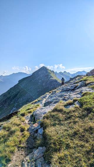 Ein Wanderer – klein im Bild – läuft auf einen langen Berggrat zu.
