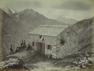 altes schwarz-weiß Bild der Olperer Hütte im Zillertal, um 1885. 4 Männer und eine Frau in Tracht vor der Hütte