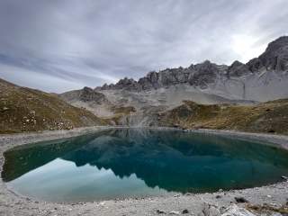 Grünblauer Bergsee mit felsigen Bergen im Hintergrund