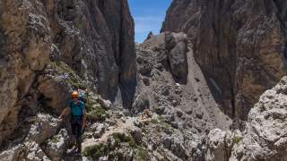 Bergsteiger geht über schmales Felsband, im Hintergrund die Langkofelscharte