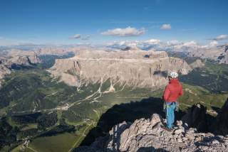 Bergsteiger steht auf ausgesetztem Gipfel mit wem Panoramablick über die Dolomiten.