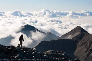 Person läuft in felsigem Berggelände, im Tal hängen Wolken