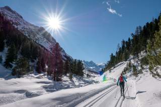 Eine Langläuferin läuft im klassischen Stil auf der Loipe durch ein Alpental.