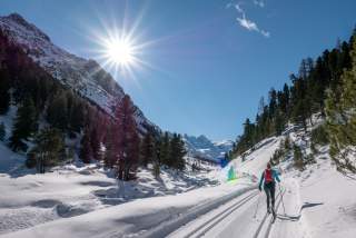 Eine Langläuferin läuft im klassischen Stil auf der Loipe durch ein Alpental.