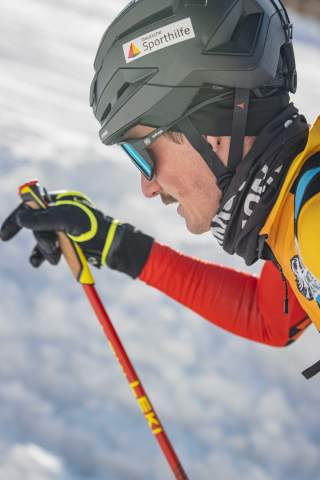 Nahaufnahme eines Skibergsteigers, im Hintergrund ist Schnee