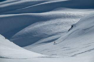 Ein Skifahrer, der alleine in hügeligem Gelände seine Schwünge zieht.