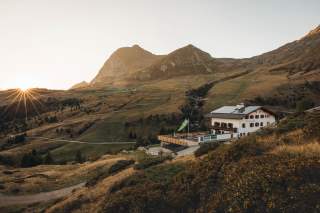 Berglandschaft bei Sonnenaufgang mit einem weißen Berghütte im Vordergrund und sanften Hügeln im Hintergrund.