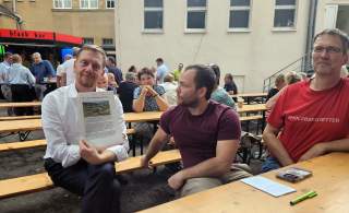 Ministerpräsident Michael Kretschmer, Toni Werner (1. Vorsitzender der DAV-Sektion Leipzig) und Mario Patzer von den „Holzberg-Rettern“ sitzen an einem Biertisch. Michael Kretschmer hält das Konzept zur Entwicklung des Holzbergs in den Händen.