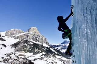 Frau am Eisklettern, im Hintergrund Berglandschaft.
