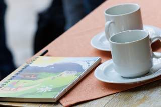 Zwei Tassen auf einem Tisch, daneben ein Block mit Illustration einer Berglandschaft